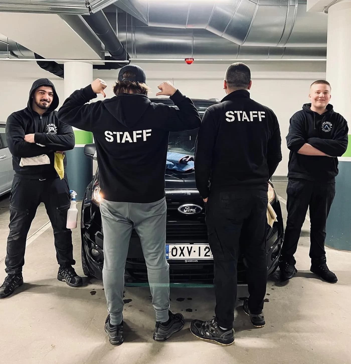 Four Premium Autopesu employees in black STAFF hoodies in front of a car in the parking garage
